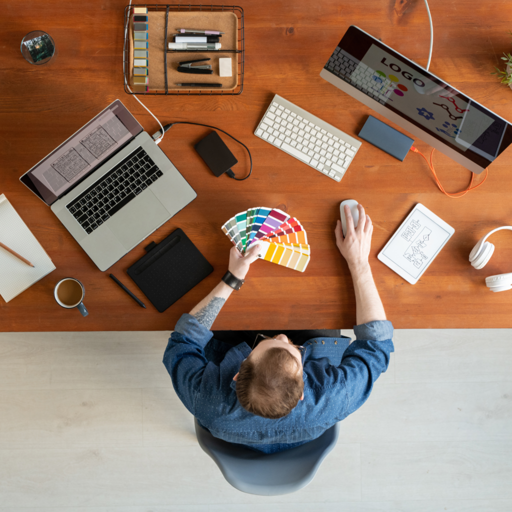 there a man surrounded with a computer monitor, laptop and work supplies doing research about our services